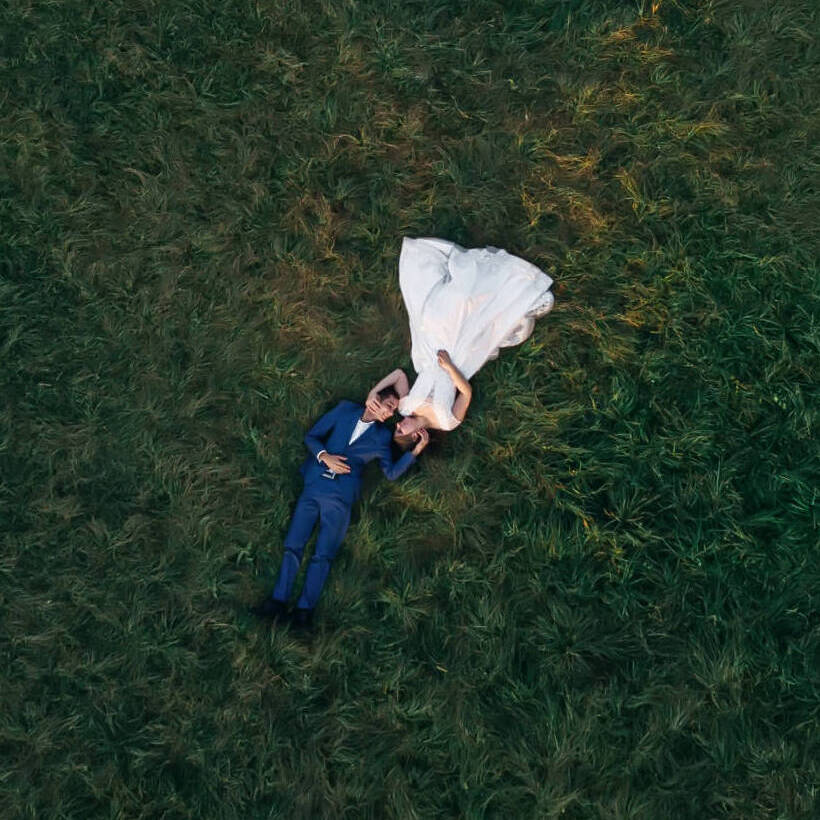 Top View Of Newlyweds Are Lying On The Grass And Looking At Each